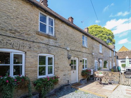A stone cottage exterior with white windows and doors with flowers in window boxes at Primrose Cottage Stow in Stow-on-the-Wold