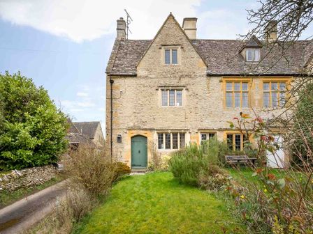 A stone house with a green door and several windows surrounded by a garden with bushes and grass at Shenley in Broadwell