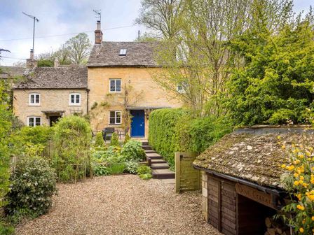 A stone house with a blue door garden plants and a gravel path at Dove Cottage Naunton