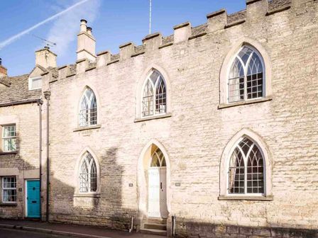 A stone building with arched windows and a white door on a street at Little Culver in Minchinhampton
