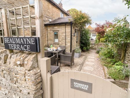 Outdoor patio area with table and chairs near a stone building at Spinners Cottage in Stow-on-the-Wold