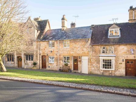 A row of stone cottages with wooden doors and windows along a street with grass and a tree at Lanes Cottage in Chipping Campden