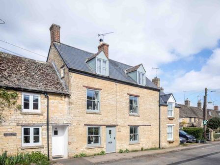 A row of stone houses with chimneys and dormer windows on a street at High Ridge in Milton-under-Wychwood