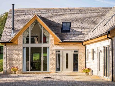 A stone house with large glass windows and a door with flower pots on each side at Flynn's Barn in Naunton