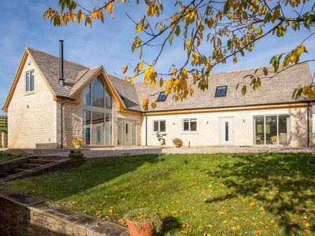 A stone house with large windows and doors surrounded by grass and trees at Hetty's Stables in Aylworth nr Naunton