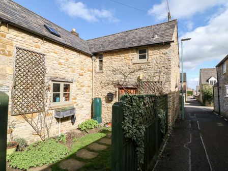 Exterior of a stone cottage with a garden and green fence along a narrow street at Carters Cottage in Stow-on-the-Wold