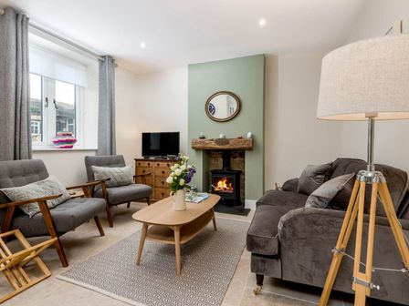 A living room with gray chairs a wooden coffee table a fireplace and a floor lamp at Wall Cottage in Burford