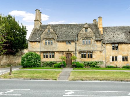 A stone house with multiple windows a wooden front door and plants in front at Little Gables in Broadway