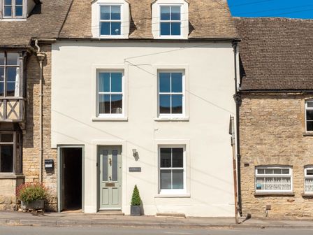A white two story house with four windows and a green door on a street at Copperbeech in Stow on the Wold
