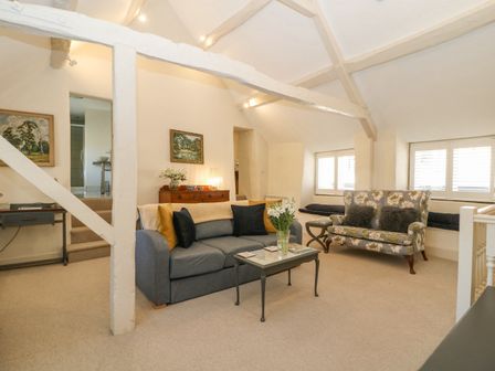 A living room with a blue sofa, floral armchair, paintings on walls, and a glass coffee table at The Apartment (Stow-on-the-Wold) in Stow-on-the-Wold