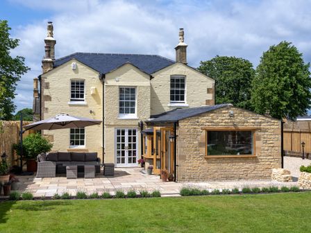 A backyard with patio furniture and umbrella next to a two-story house with stone extension at Cotsall House in Broadway