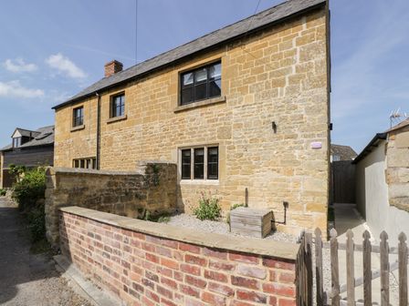 A stone house with black framed windows a brick and stone wall and a wooden gate at Millbank Cottage in Mickleton