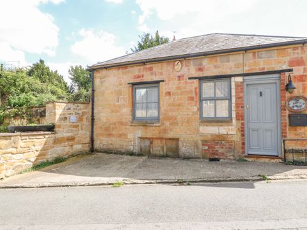 The exterior of a stone building with two windows and a door with stone walls surrounding a driveway at The Bath House in Blockley