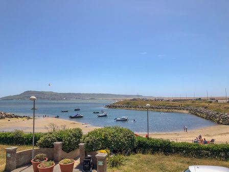 A small bay with several boats on the water a sandy beach and people near the shore with bushes and flower pots in the foreground at Beach View House in Wyke Regis