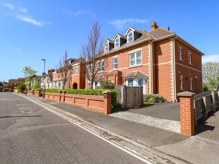 A street view of a row of attached brick houses with dormer windows and a sidewalk at Marina Reach in Weymouth