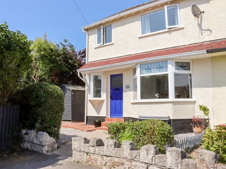 Exterior view of a two-story house with a blue front door stone wall and garden at 13 The Crescent in Rhos-On-Sea