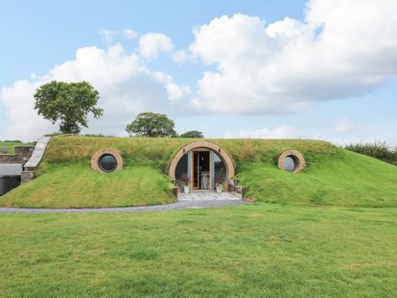 A grass covered earth house with circular windows and an arched doorway surrounded by a lawn at Tan Y Wawr - Derwen in Llanfair Caereinion