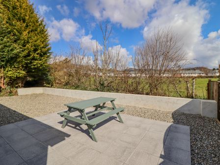 A patio with a green picnic table and gravel area next to a grass field at Mawnog Fach in Bala