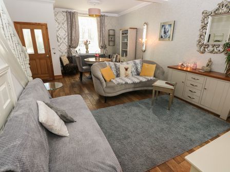 A living room with sofas a round dining table a wooden cabinet a mirror and a framed picture at 5 Pontardulais Road in Llangennech