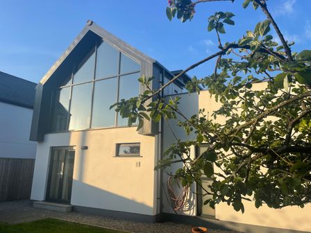 A modern house with large windows and a tree in the foreground at Avalennek in St Newlyn East