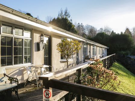 An outdoor patio area with metal chairs and tables along a building with windows and doors at Lake View in Windermere