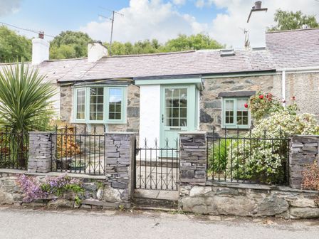 A stone cottage with green windows and door behind a black iron fence and stone pillars at Y Bwthyn Bach in Tregarth