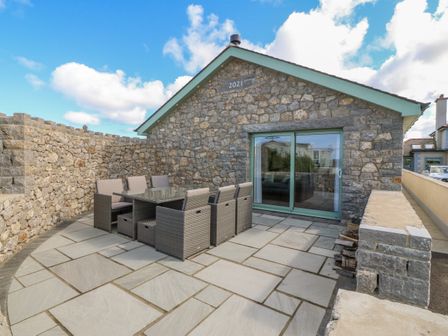 A stone patio with outdoor dining furniture in front of a stone house with sliding glass doors at Y Bwthyn in Amlwch