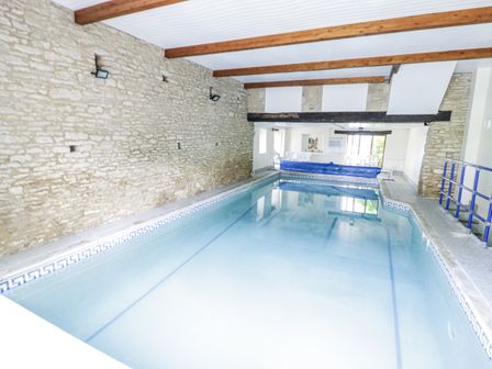 An indoor pool with stone walls and wooden beams at Dairy Cottage in Witney