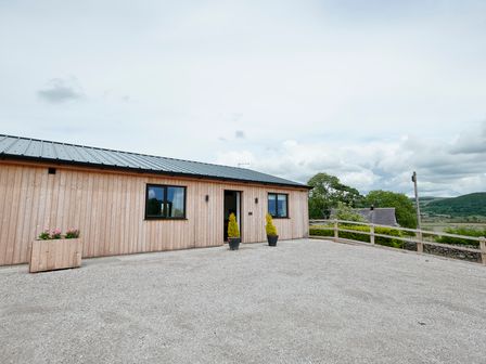 A wooden exterior building with two windows and potted plants on the gravel ground at Ingleborough Lodge in Rathmell near Settle