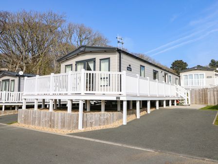 A mobile home with a white deck and railing surrounded by trees at Crosswinds 68 in Bembridge