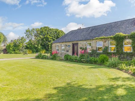 A stone house with a slate roof surrounded by a lawn and flower garden at Barnacre in Longhirst near Morpeth