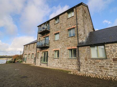 A stone building with multiple windows and small balconies near a body of water at Flat 2 in Pembroke