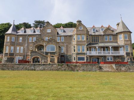 A large stone building with multiple windows and turrets on a grassy lawn at On the Straits in Glyngarth near Menai Bridge