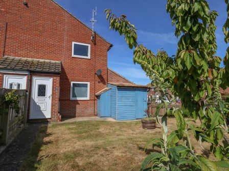 A backyard with a brick house a blue wooden shed a small fenced garden and plants at Sandpiper in Weymouth
