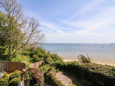 A view of the beach and sea with boats anchored offshore and greenery in the foreground at Castle Cove Cottage in Weymouth