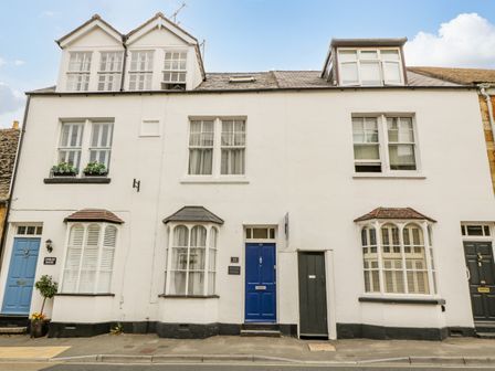 A row of white houses with blue and black doors and shuttered windows at Primrose Cottage in Winchcombe