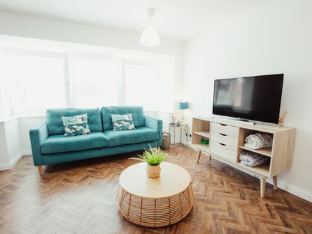 A living room with a teal sofa a round wooden coffee table and a TV on a wooden stand at Seaside House in Bridlington
