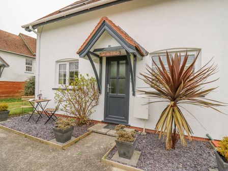 The front entrance of a white house with a dark door a small table and two chairs plants in pots and garden beds at Oak Tree Cottage in Aberporth