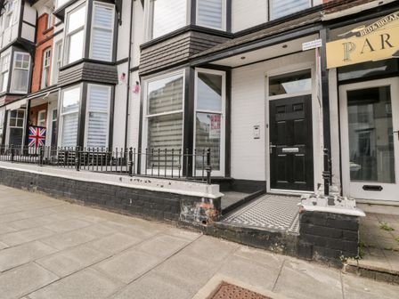 Exterior of a white brick building with black door and bay windows with metal railings on a tiled pathway at North Bay Retreat in Scarborough