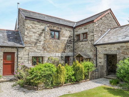 A stone cottage exterior with multiple windows red doors greenery and a gravel pathway at Nightingale Cottage in Lostwithiel