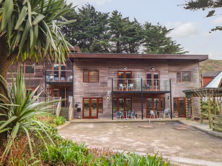 A wooden building with balconies and patio furniture surrounded by trees at Tolcarne in Porthtowan