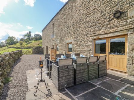 An outdoor dining area with chairs and a table set against a stone building wall at Hollowgill Barn in Sedbergh