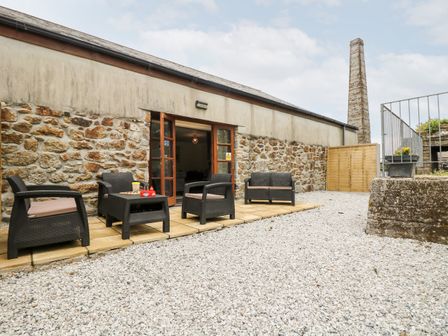 An outdoor patio with black wicker chairs and tables in front of a stone wall building at Water Wheels@The West Dry in St Austell