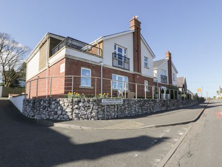 Two attached houses with brick and white walls on a corner at Llys Rhostrefor Court in Benllech
