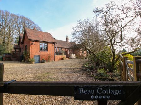 A red brick cottage with a gravel driveway and leafless trees at Beau Cottage in Bewdley