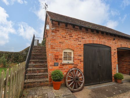 An exterior view of a brick building with black wooden doors stone steps and potted plants at The Loft Room in Dymock near Newent