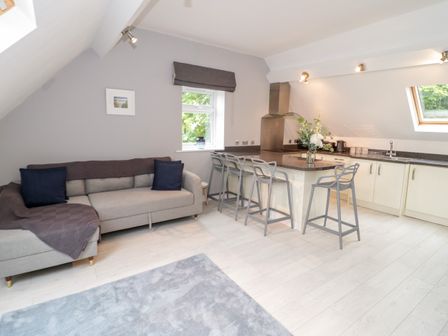 A living area with a beige sofa and gray cushions next to a kitchen island with four gray bar stools at 1 Old Kingdom Hall in Amlwch