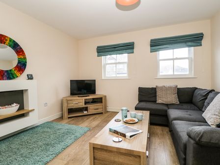 A living room with a sectional sofa a coffee table a TV on a wooden stand a rug and two windows with blinds at Fox's Retreat in Keswick
