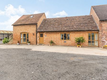 A brick building with multiple wooden doors and windows with plants outside at The Granary at Lane End Farm in Wickhamford near Broadway