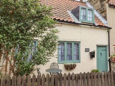 The exterior of a cottage with green framed windows and door a wooden fence a small round table with two chairs and a tree at Cholmley Cottage Ruswarp